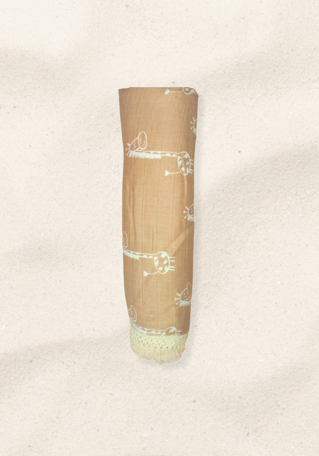 Rolled mocha-colored organic cotton baby blanket featuring white giraffe illustrations and white fringed edges, displayed on a sand background.