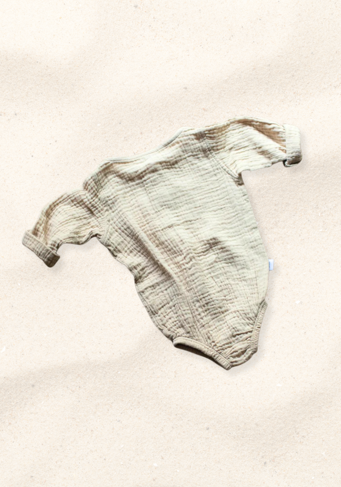 Beige long sleeve baby romper made from organic cotton with wooden buttons and snap closure, laid flat on a sand-colored background