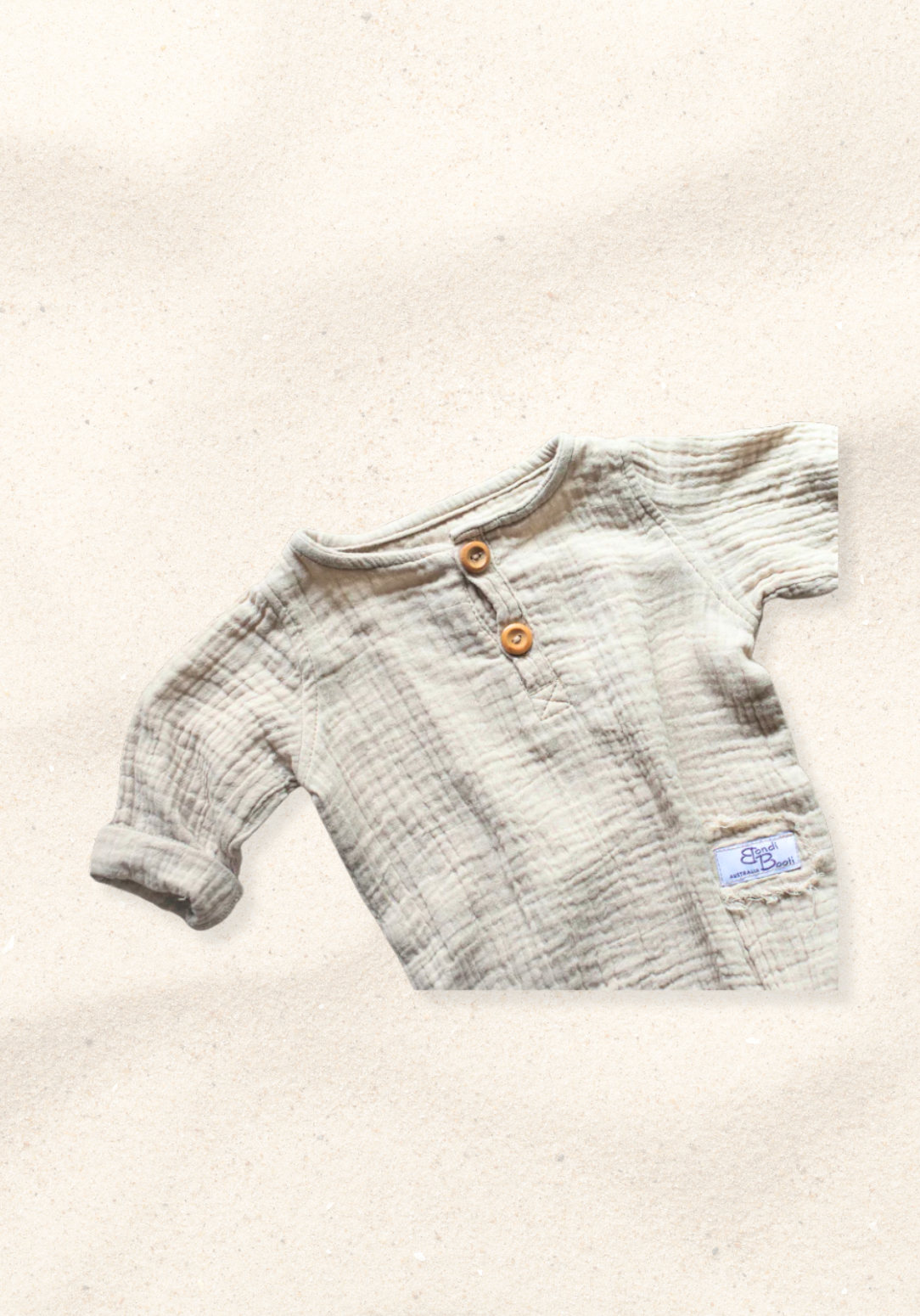 Beige long sleeve baby romper made from organic cotton with wooden buttons and snap closure, laid flat on a sand-colored background