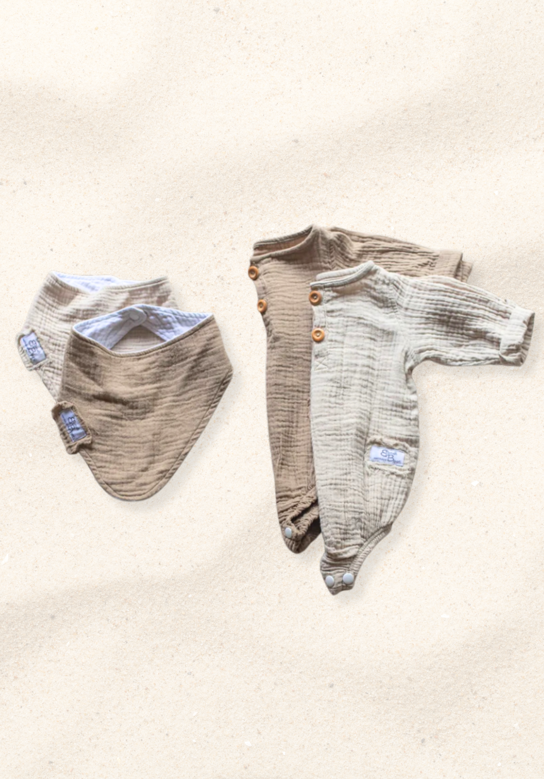 Beige long sleeve baby romper made from organic cotton with wooden buttons and snap closure, laid flat on a sand-colored background