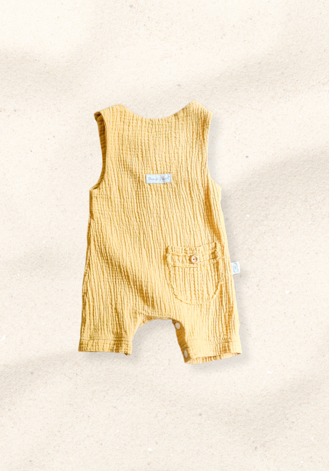 Mustard-colored organic cotton baby overall onesie with easy-change snaps on the bottom and wooden buttons on the shoulders.