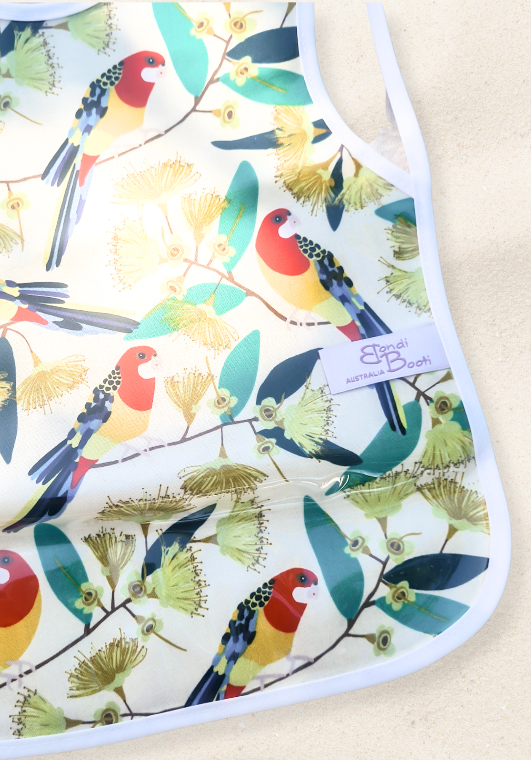 Laminated toddler feeding bib with a vibrant print of red and yellow native Australian birds perched on eucalyptus branches, white trim edges, and tie closure, displayed flat on a sand background.