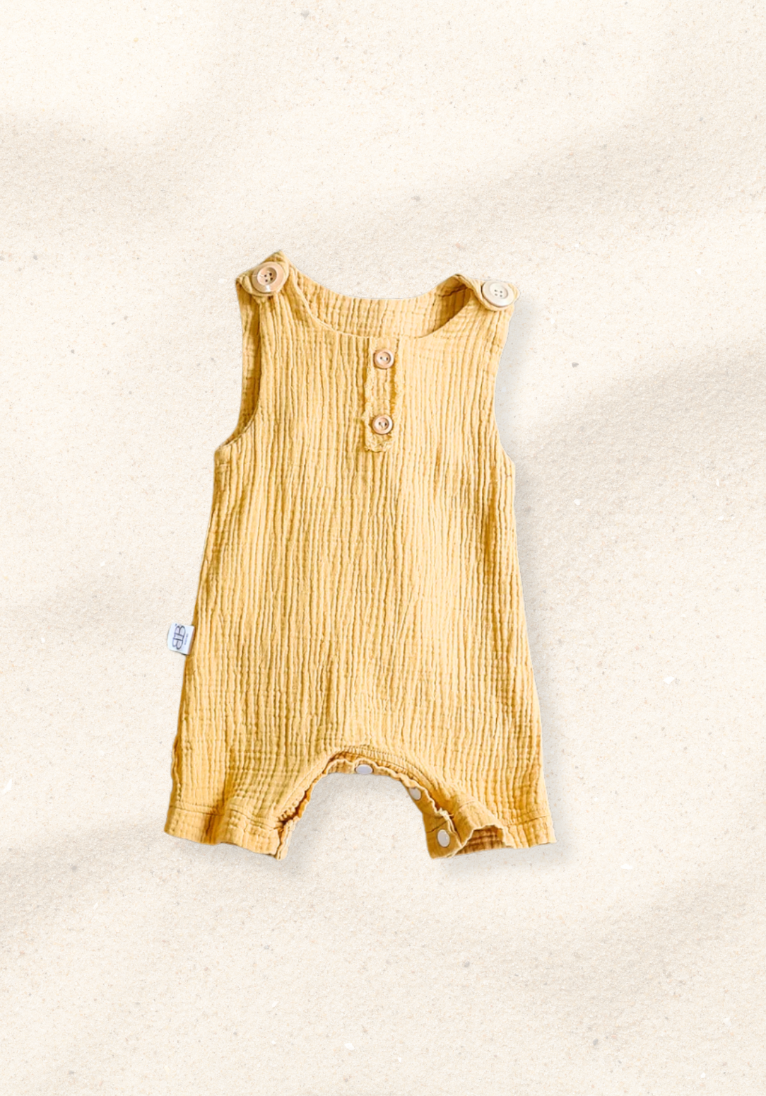 Mustard-colored organic cotton baby overall onesie with easy-change snaps on the bottom and wooden buttons on the shoulders.